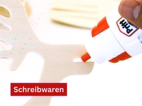 Eine rote und weiße Tube Klebestift der Marke Pritt liegt neben einem gelben Schwamm und einem weißen Papier.